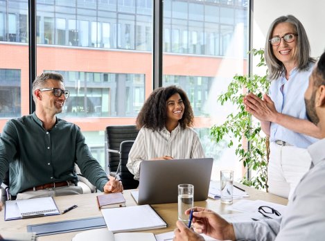 Senior older female executive ceo and happy multicultural business people discuss corporate project at boardroom table. Smiling diverse corporate team working together in modern meeting room office.